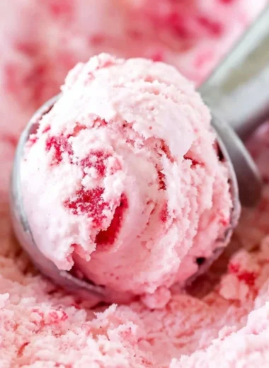 Bowl of creamy homemade strawberry ice cream topped with fresh strawberries.