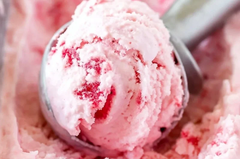 Bowl of creamy homemade strawberry ice cream topped with fresh strawberries.