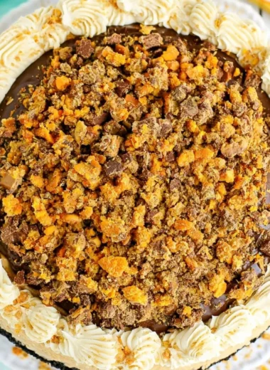 Delicious Butterfinger Cheesecake topped with chocolate and crushed Butterfinger candy.