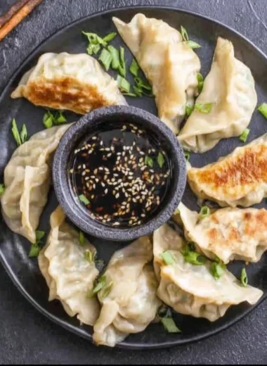 A variety of dumplings served on a wooden plate with dipping sauces.