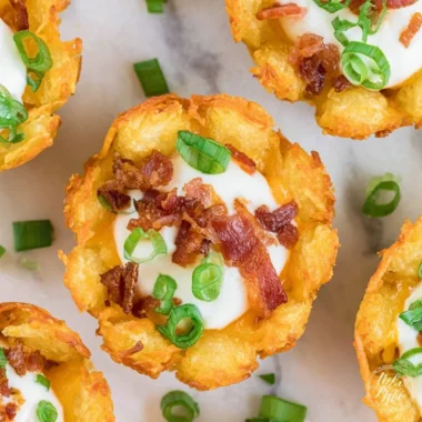 A plate of loaded tater tots topped with cheese, sour cream, and green onions.