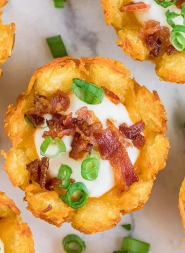 A plate of loaded tater tots topped with cheese, sour cream, and green onions.