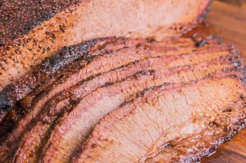 Juicy oven-cooked brisket served on a cutting board with fresh herbs.