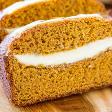 Delicious pumpkin bread with cream cheese frosting on a wooden table